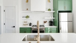 Eine moderne Küche mit grünen Schränken, weißen Arbeitsplatten, einer Edelstahlspüle und einem eingebauten Backofen.