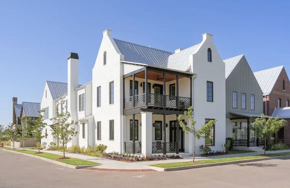 A two-story residential building with a balcony, a covered porch, and a brick chimney.