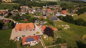 Vista aérea de un pueblo rural con casas, un edificio grande con paneles solares y campos abiertos.