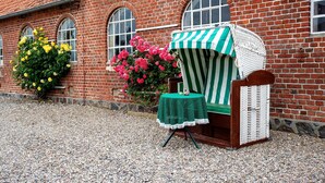 Un edificio de ladrillo con ventanas arqueadas, una silla de mimbre con funda a rayas y una mesa con mantel verde.