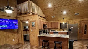 Una cocina amplia con armarios de madera, una isla central con taburetes, un refrigerador grande y un ventilador de techo.