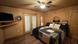 Un dormitorio con paneles de madera, una cama, un ventilador de techo, un televisor sobre una estantería y un cartel que dice 'Love House'.