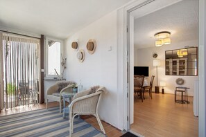 Une pièce comprenant une table à manger, des chaises, une petite table d’appoint, un fauteuil en osier, un miroir et une porte donnant sur une autre pièce.