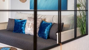 A modern living room with a sofa, cushions, a small round table, and a potted plant.