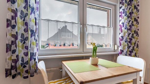 Une pièce avec une table en bois, des chaises blanches, un tapis vert et une plante en pot.