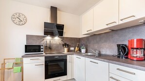 Une cuisine moderne avec des meubles blancs, un four à micro-ondes, un four traditionnel, une machine à café et une horloge murale.