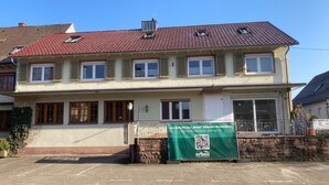 Un bâtiment à deux étages, doté d’un toit recouvert de tuiles, de nombreuses fenêtres et d’une banderole verte avec un code QR.