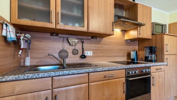A kitchen with wooden cabinets, a granite countertop, a stainless steel sink, a stove, and a microwave. - Apartment 'Kreuzstube' with Mountain View and Wi-Fi (Biberach)