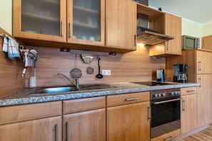 Una cocina con armarios de madera, encimera de granito, pileta de acero inoxidable, estufa y microondas.