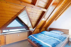 Une chambre avec un plafond en pente, une fenêtre, un radiateur et un lit avec une literie à rayures.