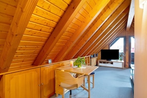 Une chambre mansardée avec des poutres en bois, une télévision, une table avec une plante et une chaise.
