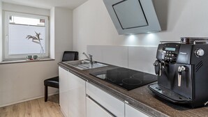 A modern kitchen with a built-in stove, a coffee machine, and a window with blinds. - Apartment 'Ferienwohnung Zur Weinsteige' with Wi-Fi (Ihringen am Kaiserstuhl)