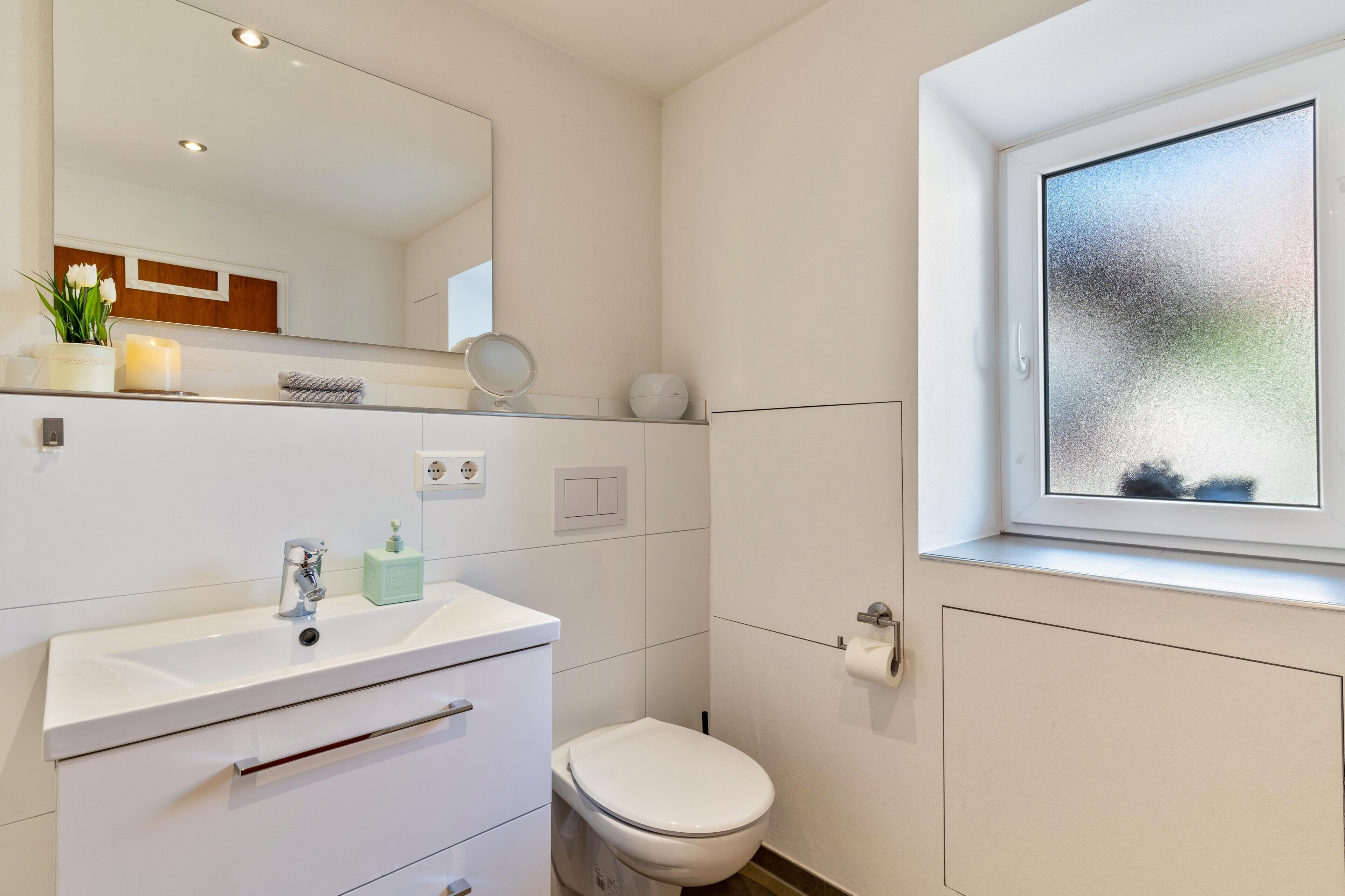 A modern bathroom with a white sink, mirror, and toilet.
