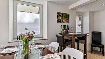 Un comedor con una mesa de madera dispuesta para cuatro personas, sillas blancas, un jarrón con flores y un cuadro en la pared.