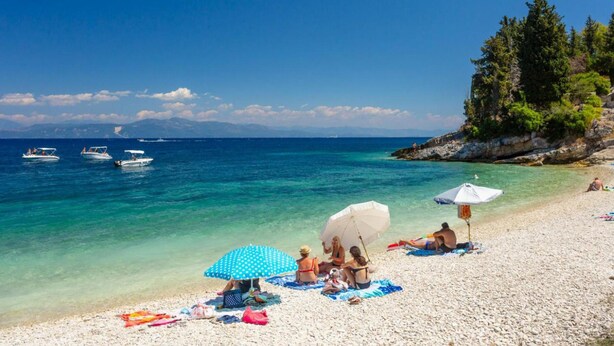 Een strand met helder turquoise water, boten en mensen die ontspannen onder parasols.