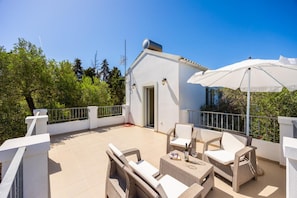 Ein Balkon mit Korbmöbeln, einem weißen Sonnenschirm und einem Gebäude mit Tür und Fenstern.