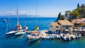 A marina with various boats docked, a building with a tiled roof, and a clear blue sky. - Agathi Cottage in Longos (Paxos)