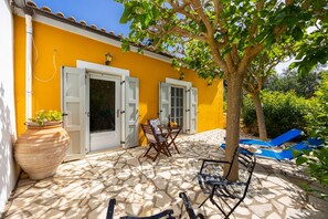 A yellow building with white shutters, a tiled patio, and outdoor furniture.
