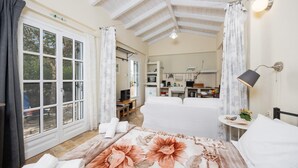 A bedroom with a large bed, a desk, and a kitchenette in the background. - Agathi Cottage in Longos (Paxos)