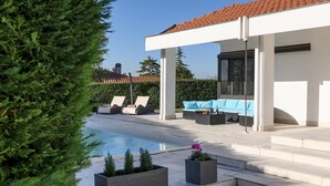 Un espace piscine extérieur moderne, doté de chaises longues et d’un coin salon abrité.