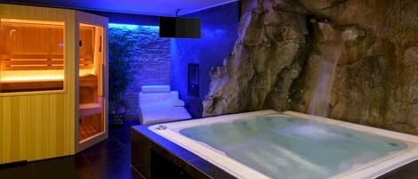 A spa area with a hot tub, wooden seating, and a stone wall with a waterfall feature.