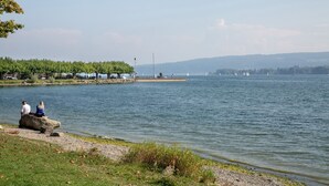 Un lago con barcos, un muelle y personas sentadas sobre una roca.