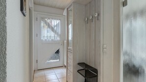 Un pasillo con una puerta blanca, un pequeño estante y vistas de una escalera.