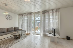 Uma sala de estar com sofá, mesa de centro, TV e cortinas.