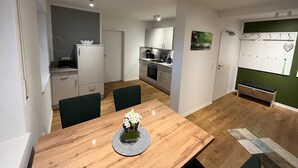Een moderne keuken met witte kasten, een eettafel met stoelen en een kleine koelkast.