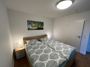 Makuuhuone, jossa on sänky, yöpöytä, seinään kiinnitetty lamppu, ovi ja kattovalaisin.