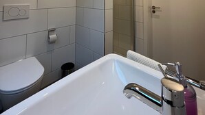 A modern bathroom with a white sink, toilet, and shower area. - Seeterrasse Apartment: Ideal for Cycling, Walks & Relaxation by the Versmolder Seenplatte (Versmold)