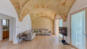 A spacious living area with a high arched stone ceiling, a large window, and a modern sofa with cushions. - Villa Porta Azzurra 6 2 Emma Villas (Salve)