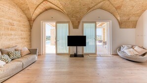 A spacious living room with a flat-screen TV, a sofa with patterned cushions, and a round seating area with cushions. - Villa Porta Azzurra 6 2 Emma Villas (Salve)