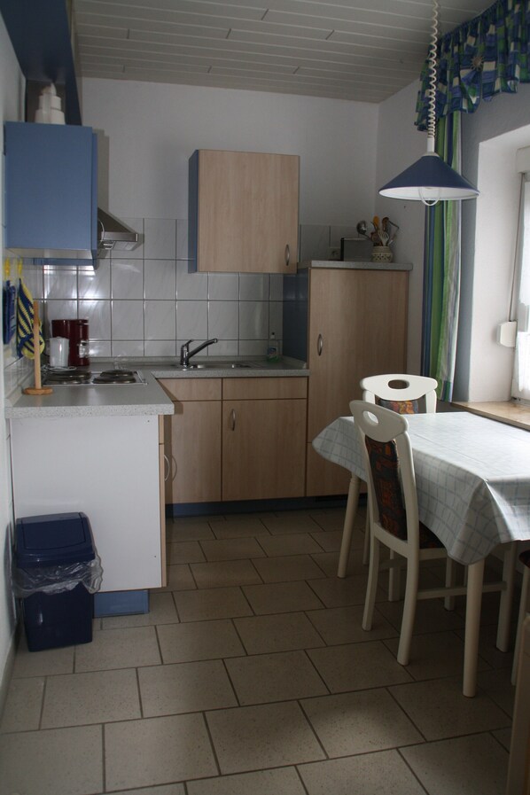 A compact kitchen with a sink, wooden cabinets, a dining table with chairs, and a ceiling fan.