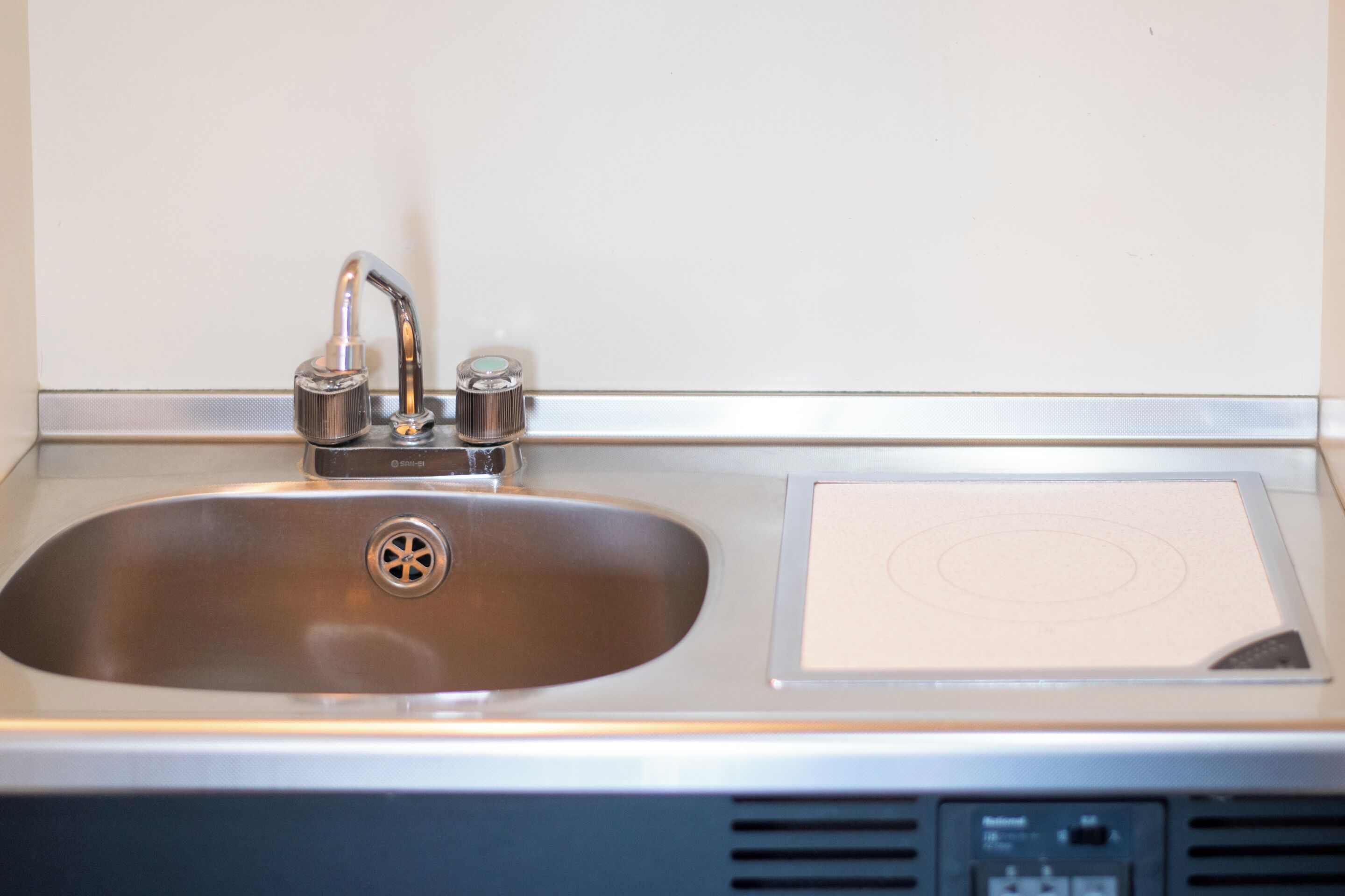 A stainless steel sink with a single faucet and a paper towel dispenser.
