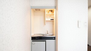 Una cocina compacta con lavavajillas integrado, un refrigerador pequeño y un estante con utensilios de cocina.