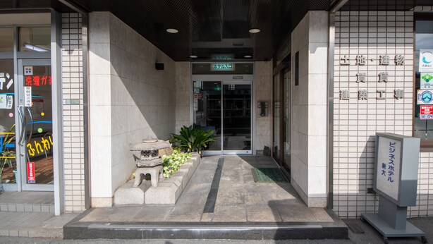 Fachada de edificio con azulejos, un pequeño jardín con plantas y un cartel.