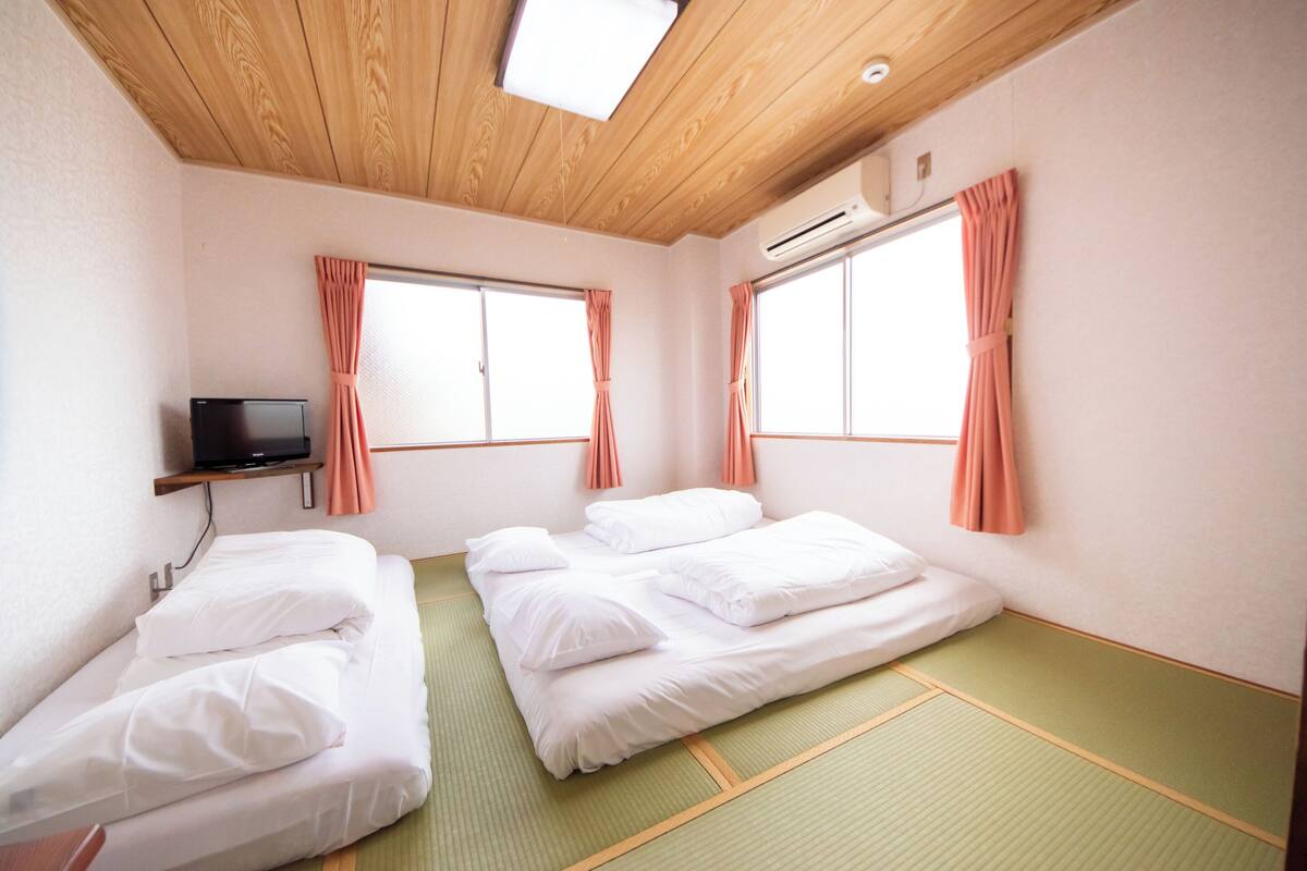 Une chambre d’hôtel avec deux lits, un téléviseur posé sur une étagère et un appareil de climatisation.