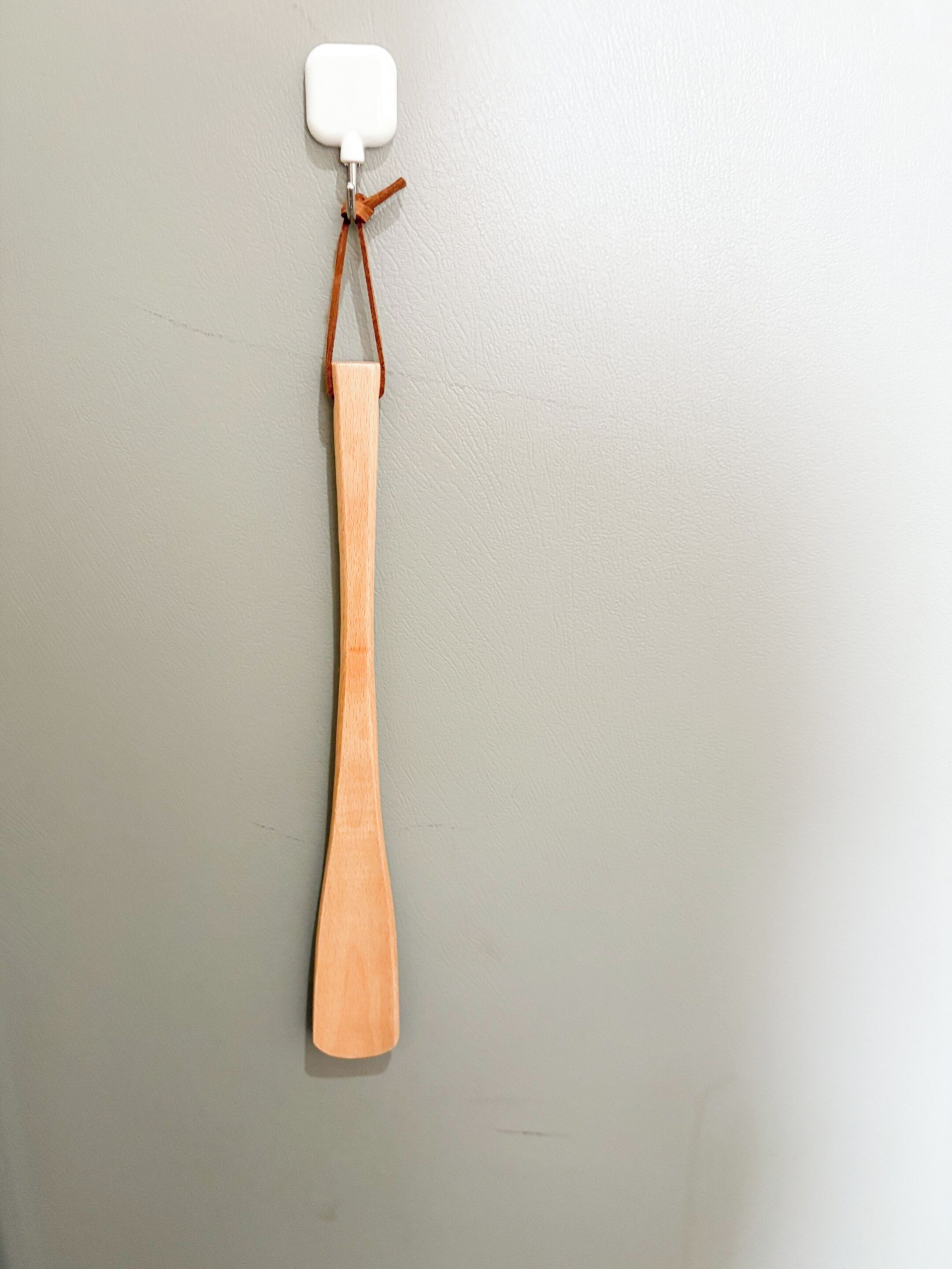 Un objeto de madera con una parte superior blanca, atado con un hilo marrón, colgando de una pared con textura.