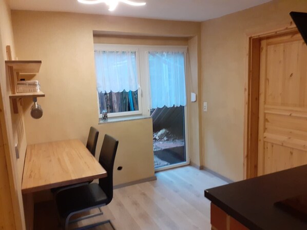 A small kitchen with a dining table and chairs, a window with curtains, and a wooden door.