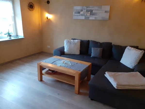 Una sala de estar con un sofá de color oscuro, una mesa de centro de madera y una lámpara fijada a la pared.