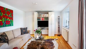 Ein Wohnzimmer mit einer Couch, einem Couchtisch mit einer Vase, einem Bücherregal und einem Fernseher.