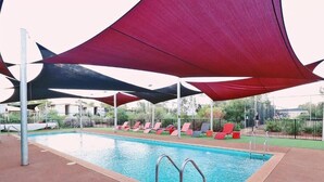 Una piscina con zona de borde, incluyendo sillones de descanso y una pérgola con sombra.