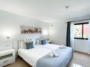 Quarto de hotel com duas camas, uma obra de arte na parede, luminárias de cabeceira, uma janela com cortinas e vista para edifícios.
