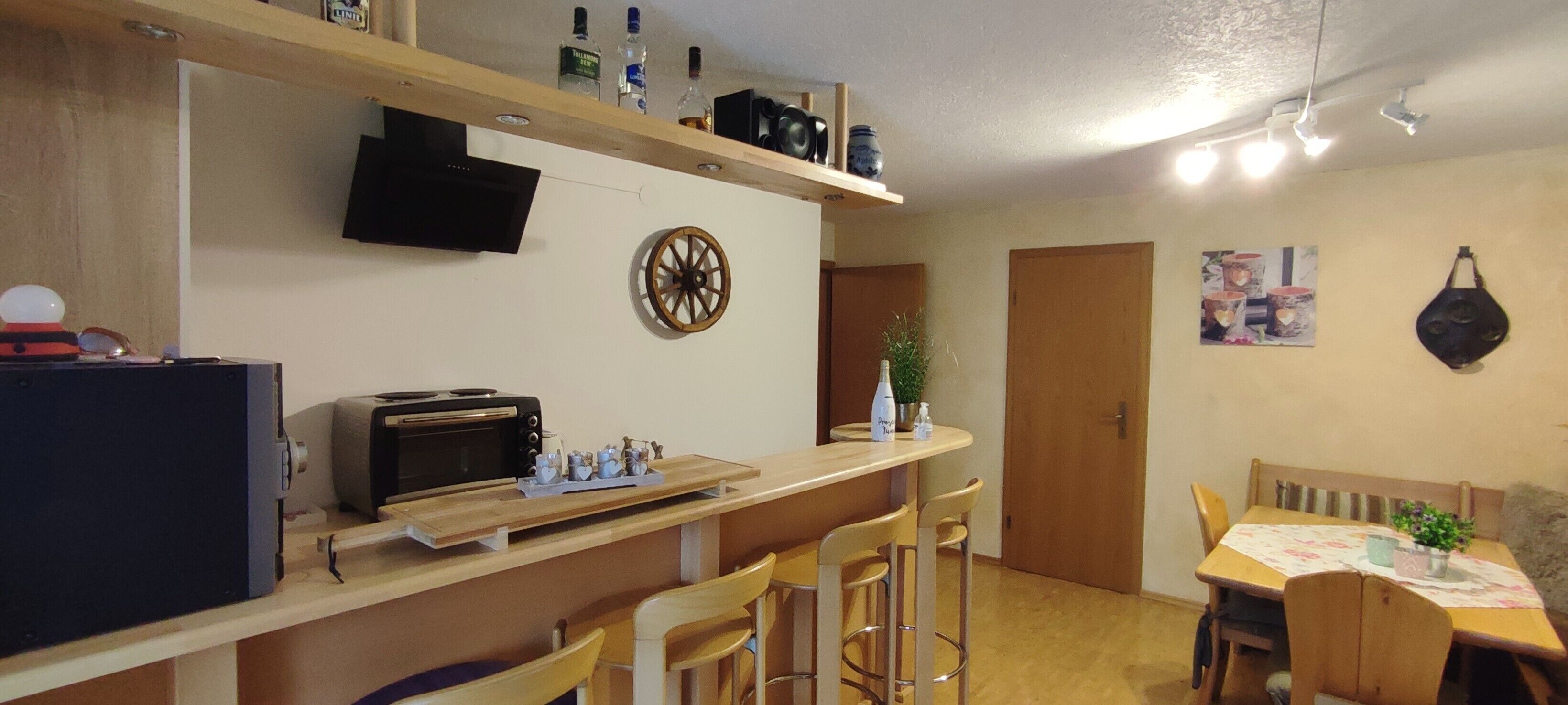 La cuisine est équipée d’un four à micro-ondes, d’un grille-pain et d’un comptoir-bar en bois. On y trouve également un téléviseur fixé au mur, une porte et une table avec des chaises.