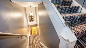 Una escalera con alfombra a rayas y un moderno aparato de luz.