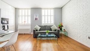 Una sala de estar moderna con un sofá gris, una mesa de centro de vidrio y una pared de ladrillo blanco.