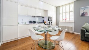 Una cocina moderna con armarios blancos, una mesa de comedor de vidrio y sillas blancas.