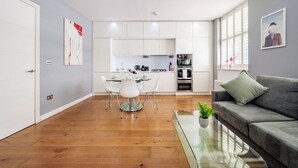 Una sala moderna con una mesa de centro de vidrio, un sofá gris y un comedor con una mesa de vidrio y sillas blancas.