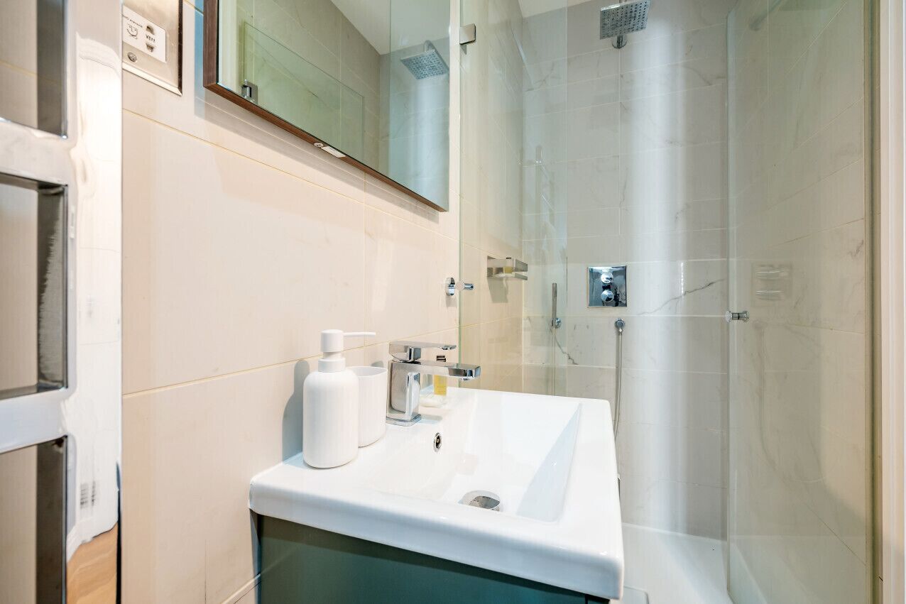 Un baño moderno con un lavamanos blanco, cabina de ducha de vidrio y un espejo sobre el lavamanos.